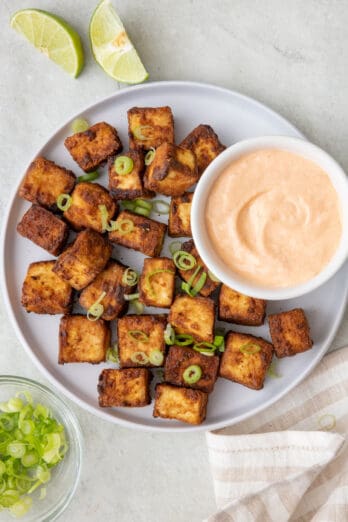 Large serving platter with tofu along with small dipping bowl for spicy mayo with lime wedges nearby and garnished with sliced scallions.