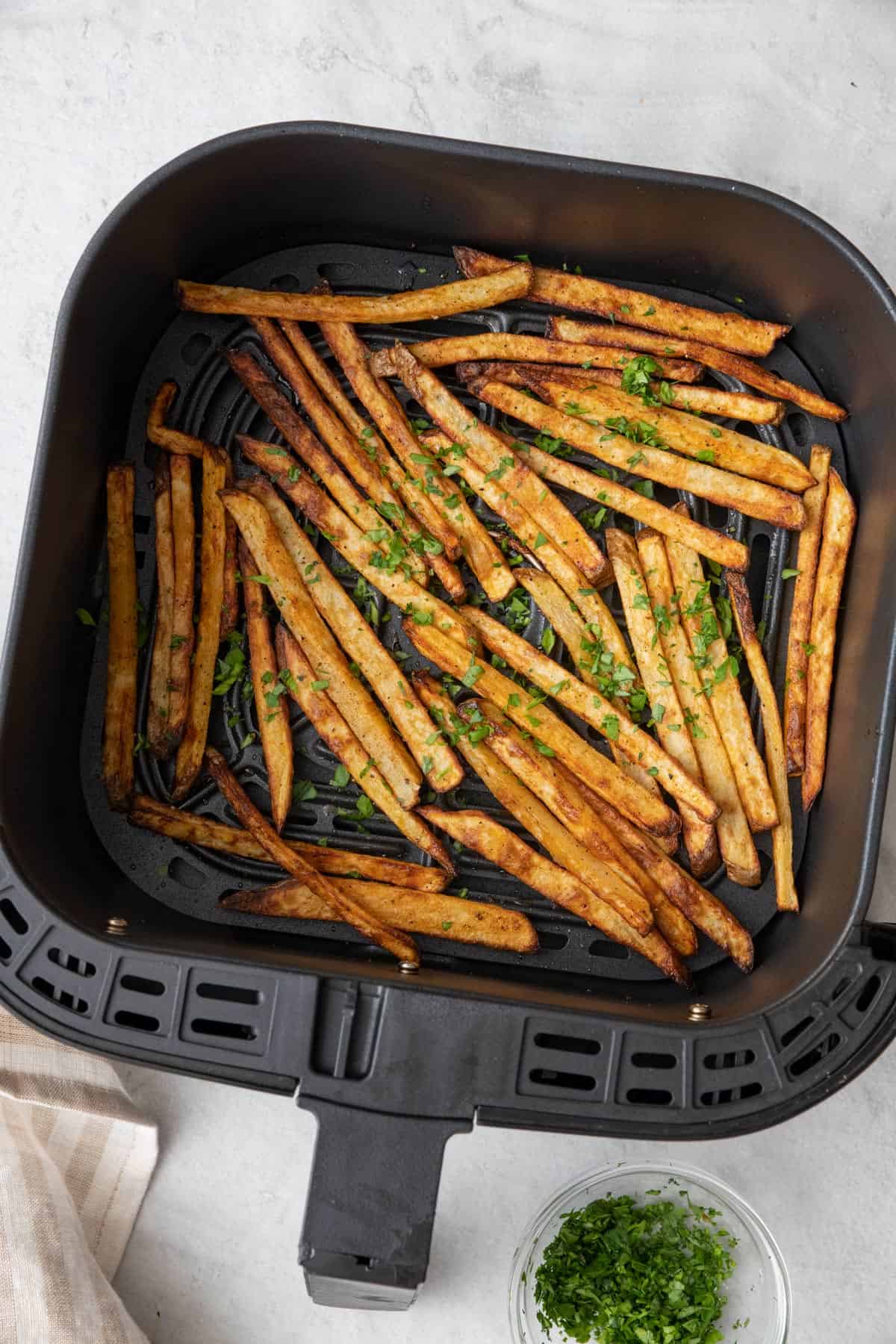 Fries in an air fryer basket garnished with fresh parsley.