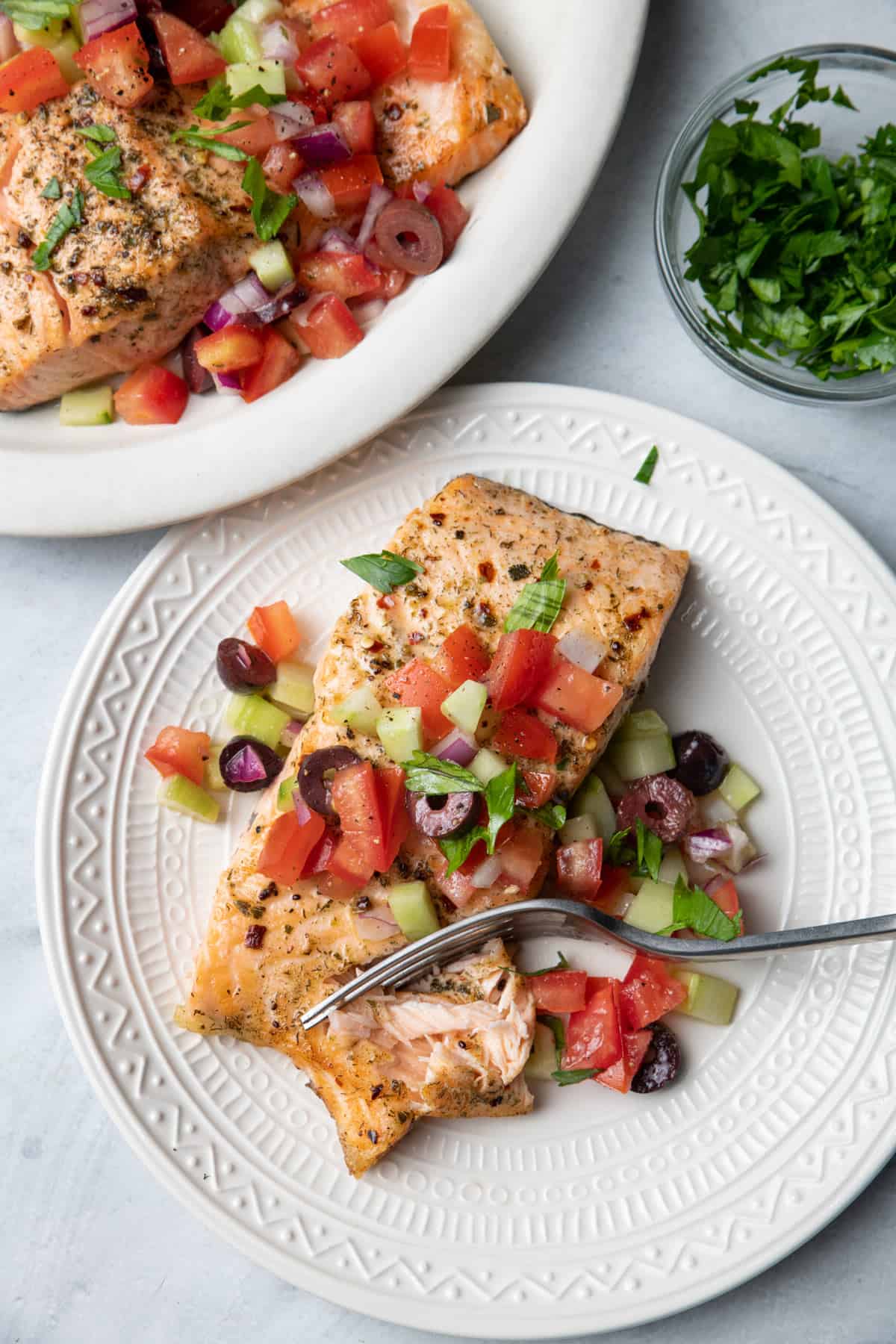 Plate of salmon cooked in air fryer, topped with greek salad