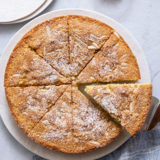 Cake cut into 8 slices on round plate, dusted with powder sugar, with cake server pulling one slice out.