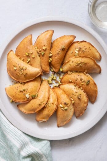 top view of round plate with baked atayef sprinkled with crushed pistachios