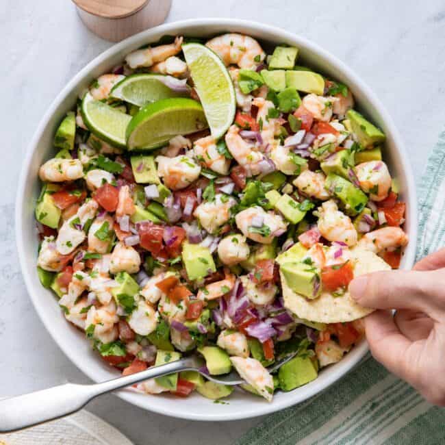 Large serving bowl of Shrimp avocado salsa with hand taking out a bite on a tortilla chip.