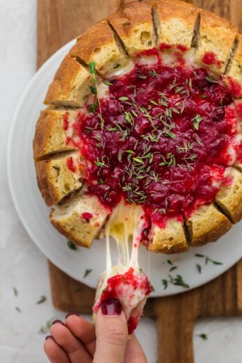 Baked brie cranberry in bread bowl after baked. Slice of bread being pulled away