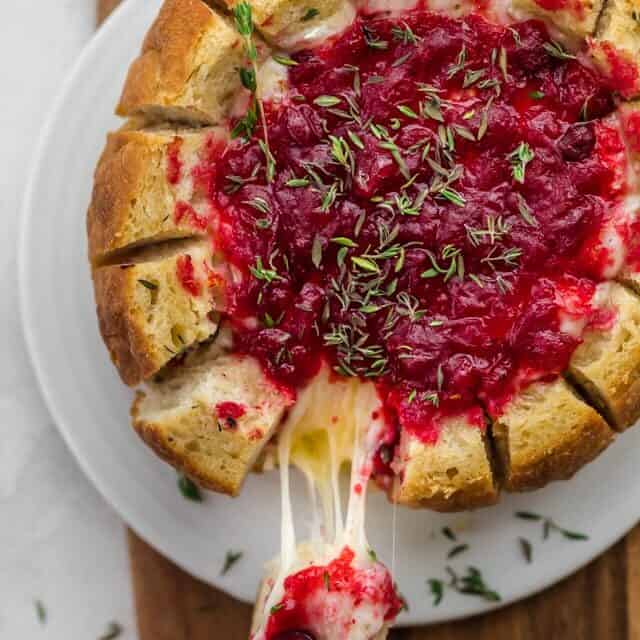 Baked brie cranberry in bread bowl after baked. Slice of bread being pulled away