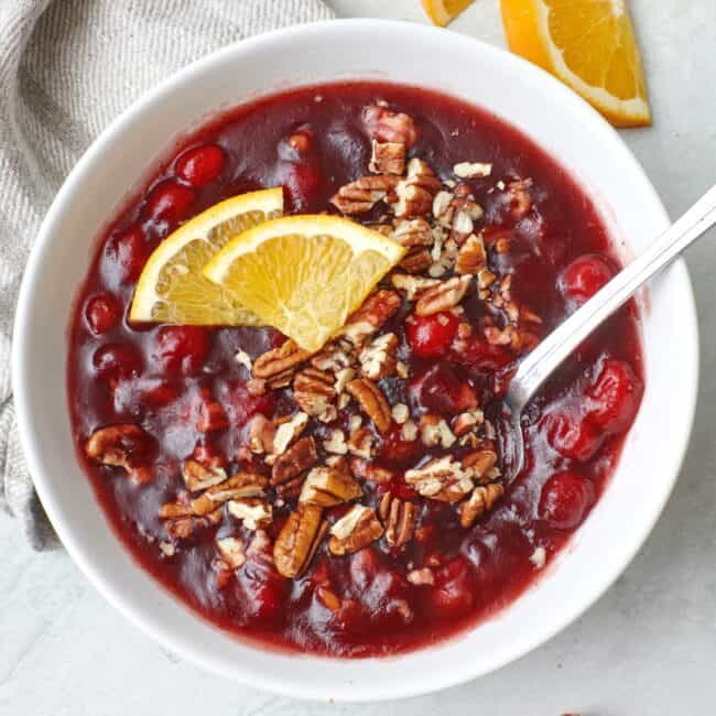 Baked Cranberry Relish in a white bowl and spoon, garnished with orange slices and pecans