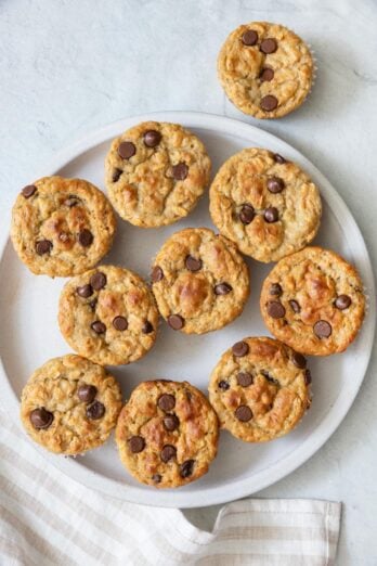 Overhead view of chocolate chip muffins on a large plate with one off to the side.