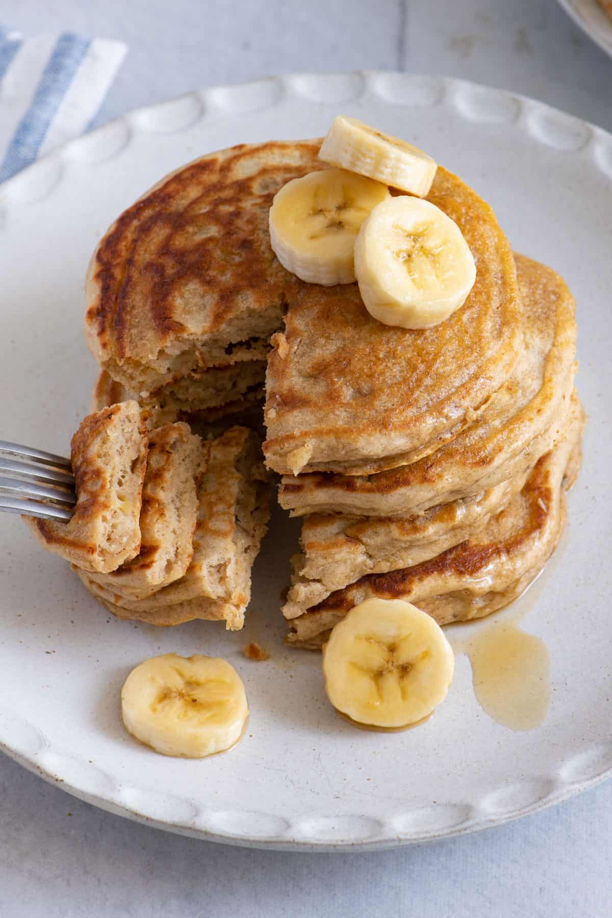 Fork taking out a cut stack from a plate of banana pancakes.