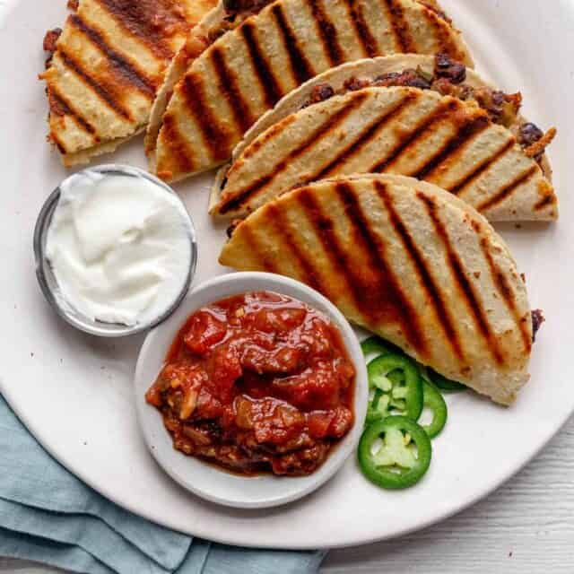 4 small bean and cheese quesadillas on a plate served with sour cream and salsa