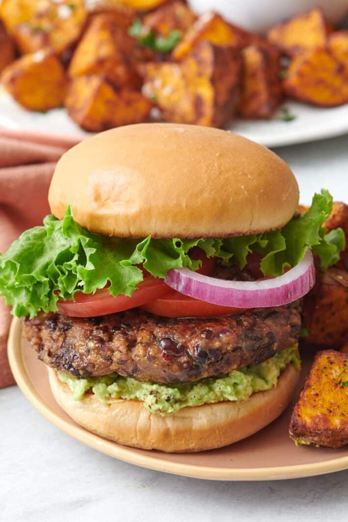 Large black bean burger on a bun with mashed avocado, tomato slices, red onion, and lettuce.