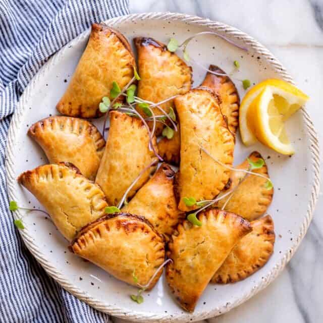 Final plated dish of the broccoli and cheese hand pies on a white plate with garnish and lemon slices