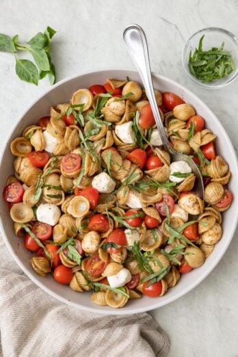 Caprese pasta salad in a large serving bowl with a spoon dipped in and extra sliced fresh basil sprinkled on top.