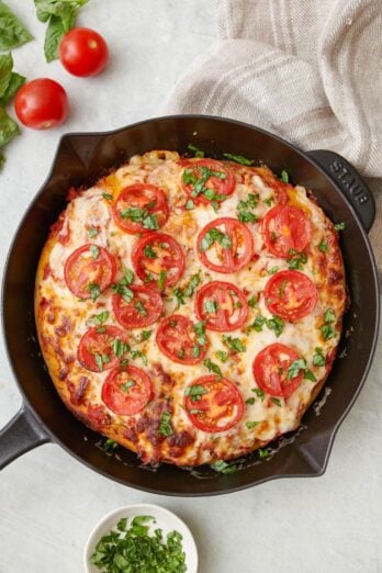 Cast iron pizza in skillet garnished with fresh chopped basil.