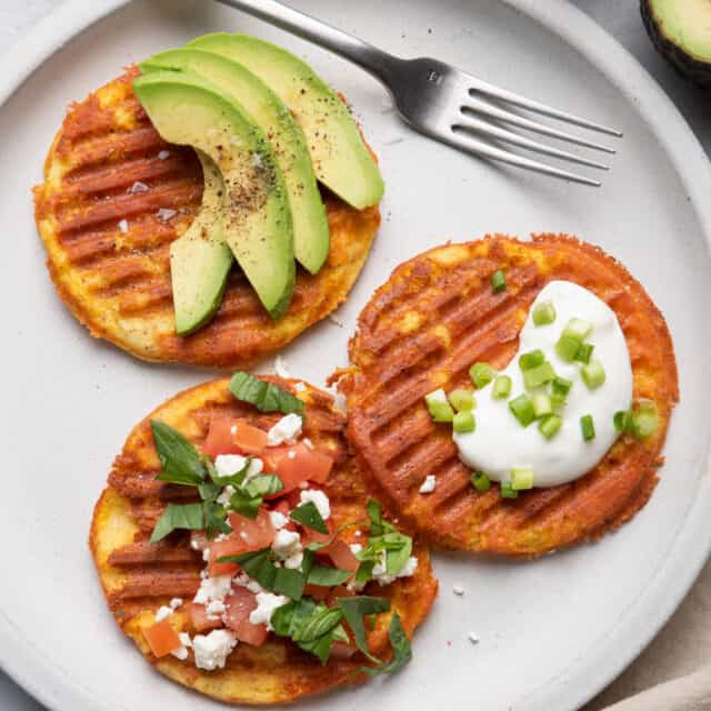 Three yogurt waffles on a plate with toppings added on top and fork on plate