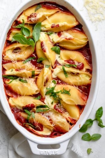 Cheese stuffed shells in a white oval baking dish topped with fresh basil