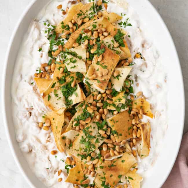 Large serving platter of chicken fatteh topped with pita, pine nuts and parsley