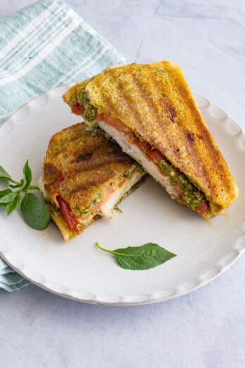 Pesto Chicken Panini cut in half on large white plate.