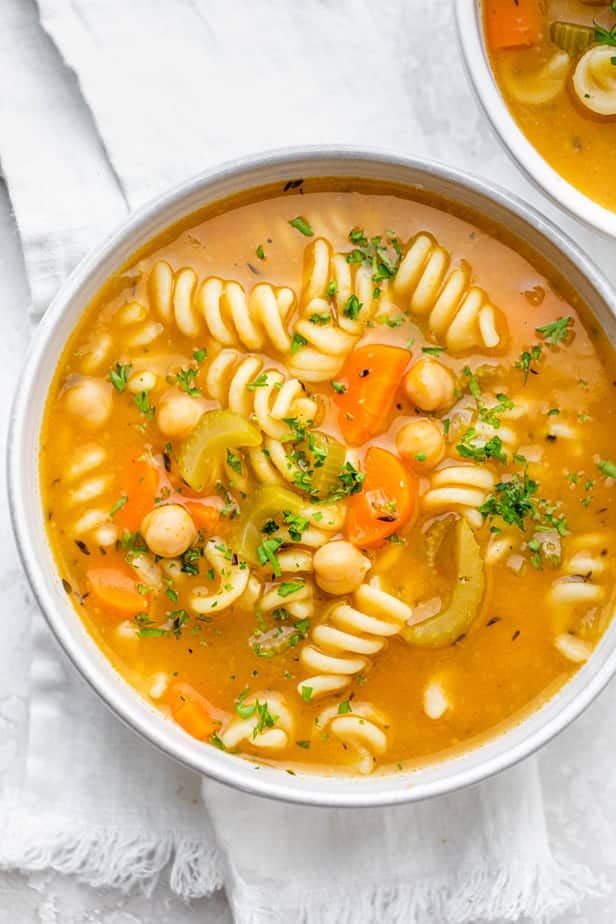 Large bowl of vegetarian chickpea noodle soup on white background