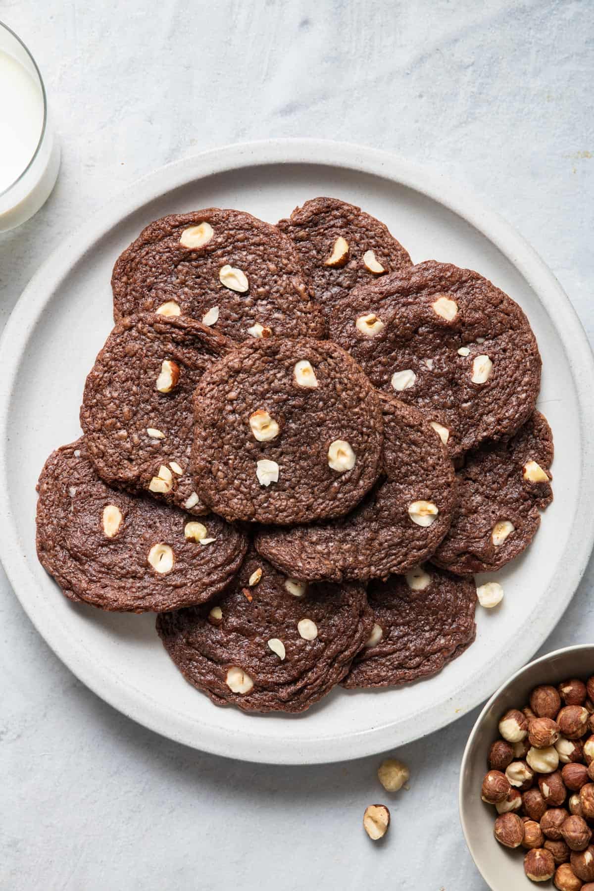 A plate of chocolate hazelnut cookies with a glass of milk