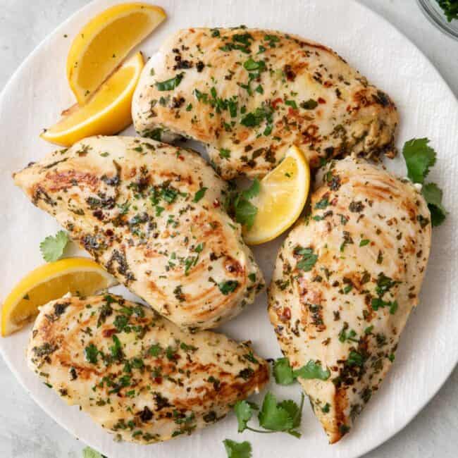 Cilantro chicken breast on a plate with extra fresh cilantro and lemon wedges.