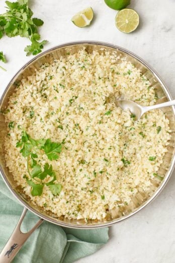 Cilantro lime cauliflower rice in a skillet with a spoon dipped in.