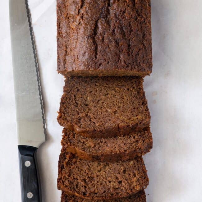 Half a loaf of Apple Bread sliced into thick pieces with remaining loaf uncut with a knife nearby.