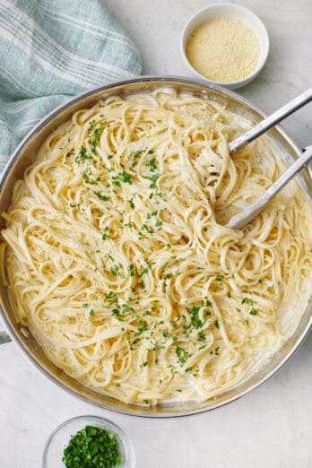 Cottage cheese alfredo pasta in a pot with tongs tucked into the pasta, garnished with fresh chopped parsley.