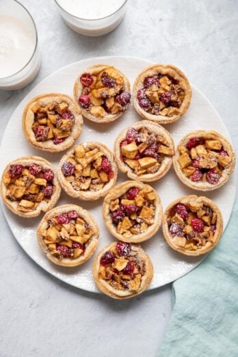 Mini cranberry apple pies on a white dish dusted with powdered sugar