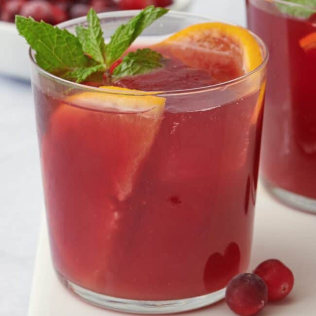 Cranberry orange mocktail in a glass with orange slices and fresh mint leaves.