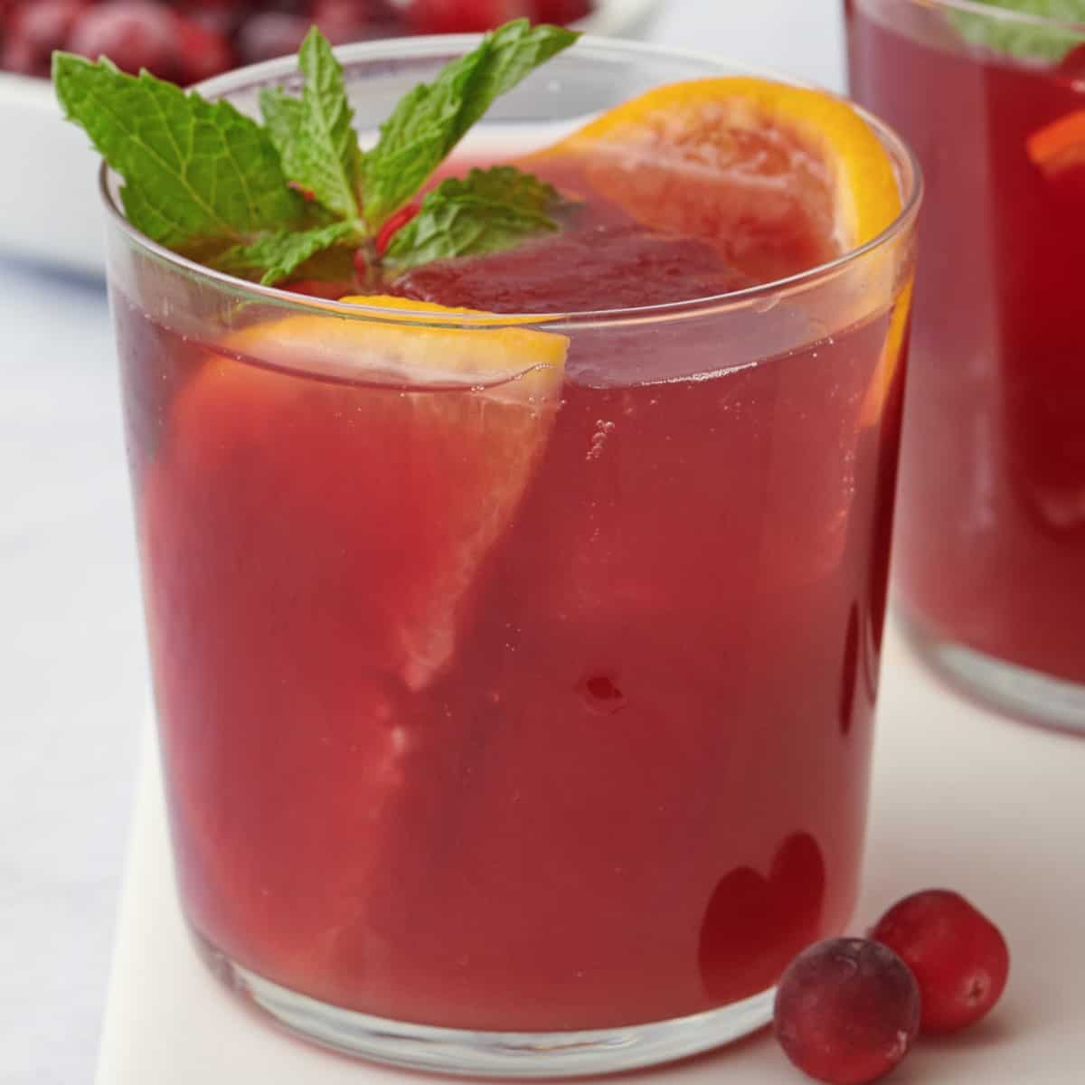 Cranberry orange mocktail in a glass with orange slices and fresh mint leaves.