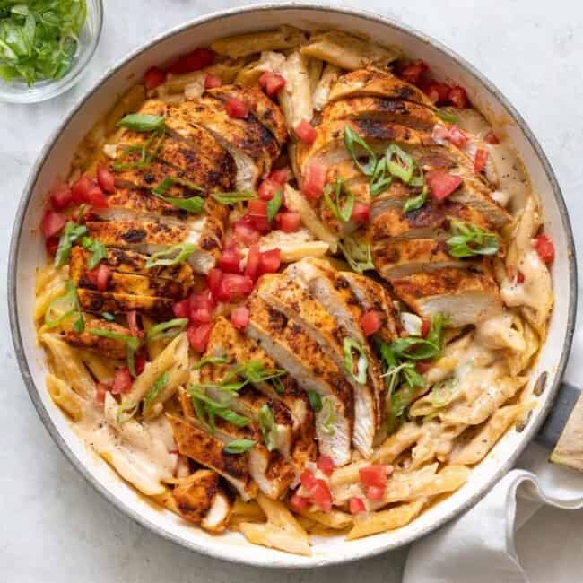 Skillet of the creamy cajun pasta garnished with roma tomatoes and green onions.