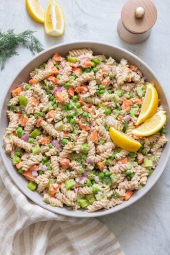 Large serving bowl filled with tuna pasta salad garnished with lemon wedges.