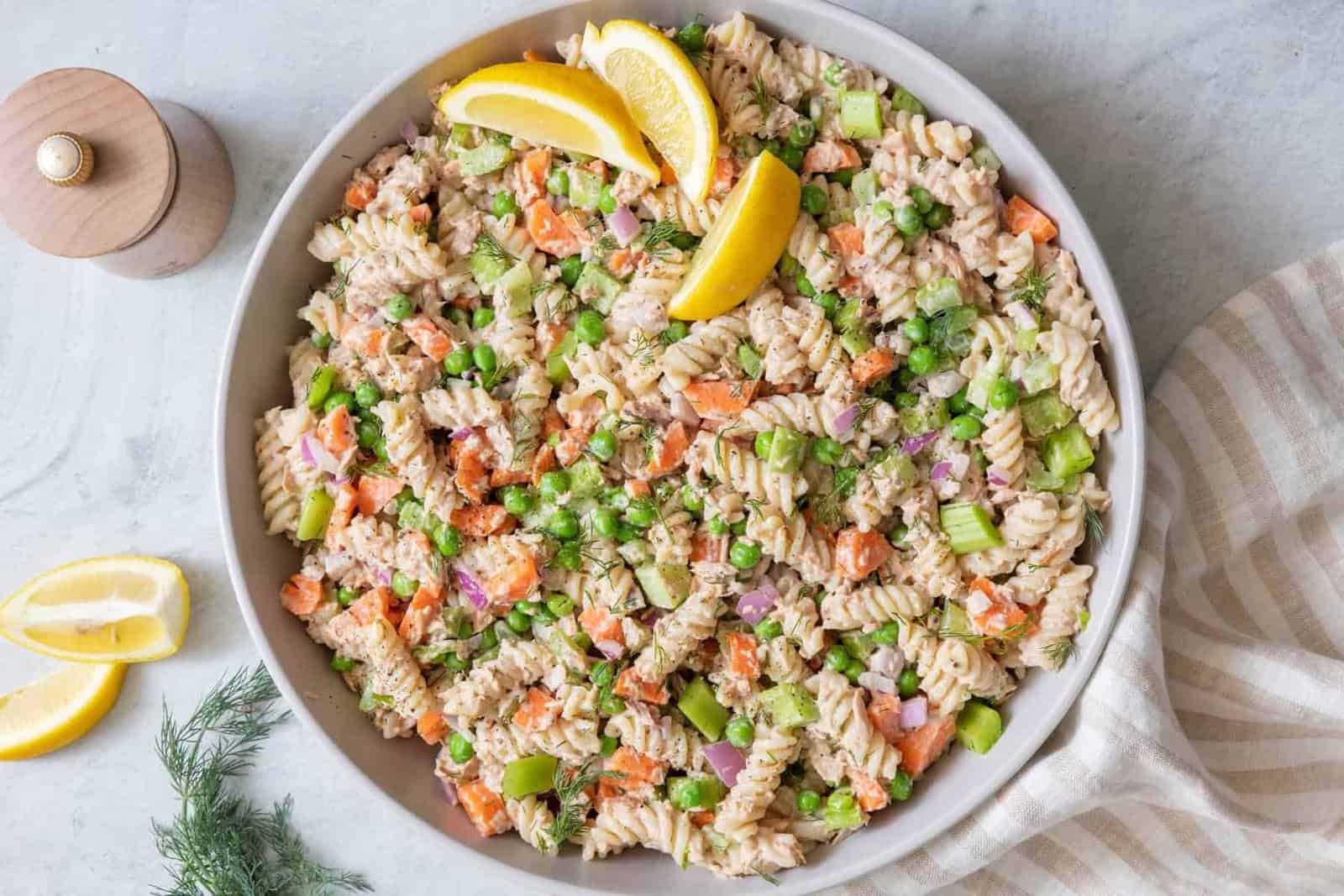 Large serving bowl filled with tuna pasta salad garnished with lemon wedges.