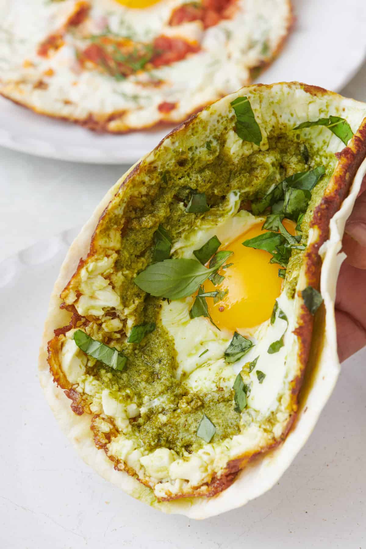 Hand holding a pesto crispy fried feta and egg on a tortilla shell slightly folded in half.