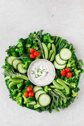 Festiva crudite platter wreath for Christmas made with kale, green beans, broccoli, snap peas, cucumbers and cherry tomatoes