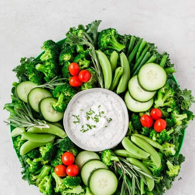 Festiva crudite platter wreath for Christmas made with kale, green beans, broccoli, snap peas, cucumbers and cherry tomatoes