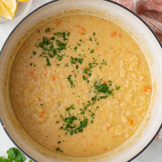 Pot of crushed lentil soup garnished with fresh parsley with lemon wedges nearby.