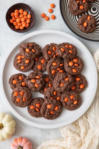 Plate of cookies on large white plate with orange candies nearby and a black and white swirl plate with a few cookies on it.