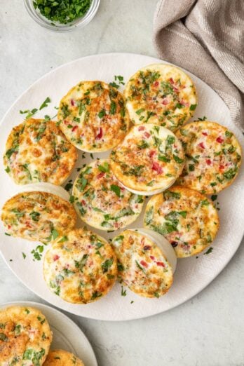 Egg white bites on a plate with 2 on a smaller plate nearby, garnished with fresh parsley.