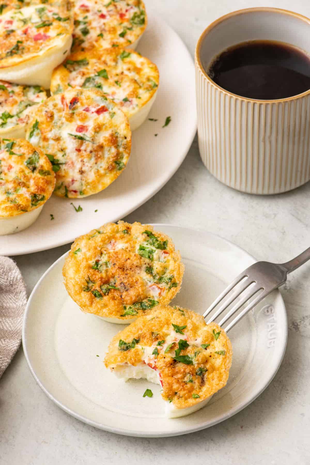 Two egg white bites on a small plate with a bite taken out of one. Plate of more and a cup of coffee nearby.