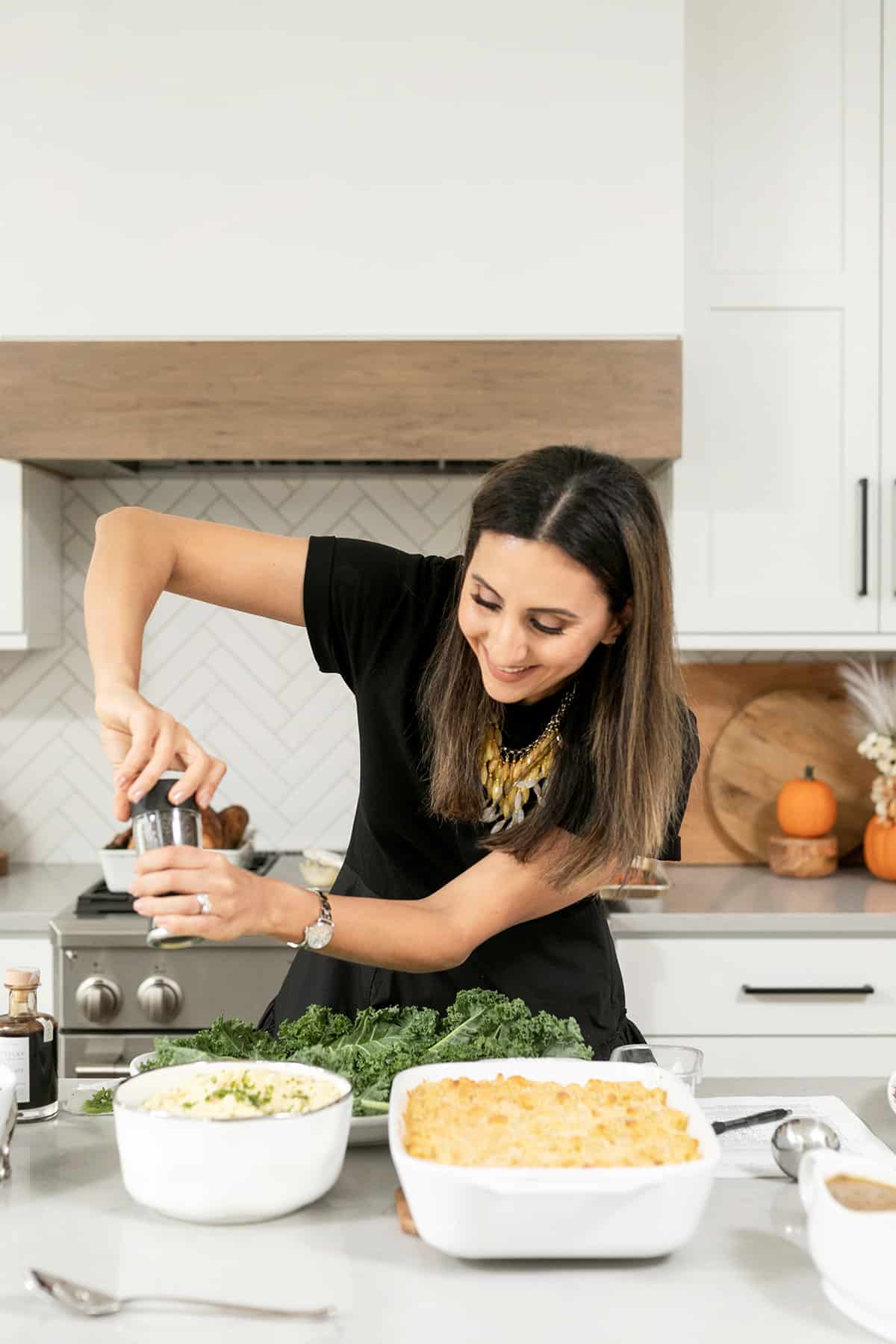 Yumna seasoning mashed potatoes in a serving bowl nexty to baked macaroni and cheese and a large turkey platter with kale leaves.