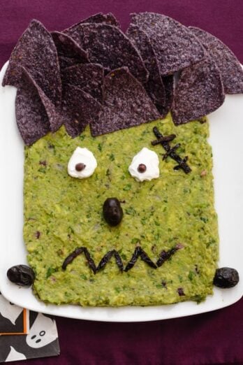 Frankenguac Halloween guacamole decorated with tortilla chips, olive and sour cream