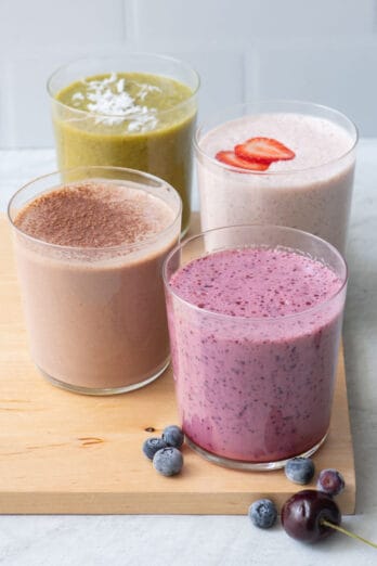 4 different smoothie recipes in short glasses sitting on wood board.