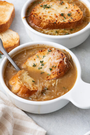 Spoon cutting into cheese bread and scooping some French onion soup up.