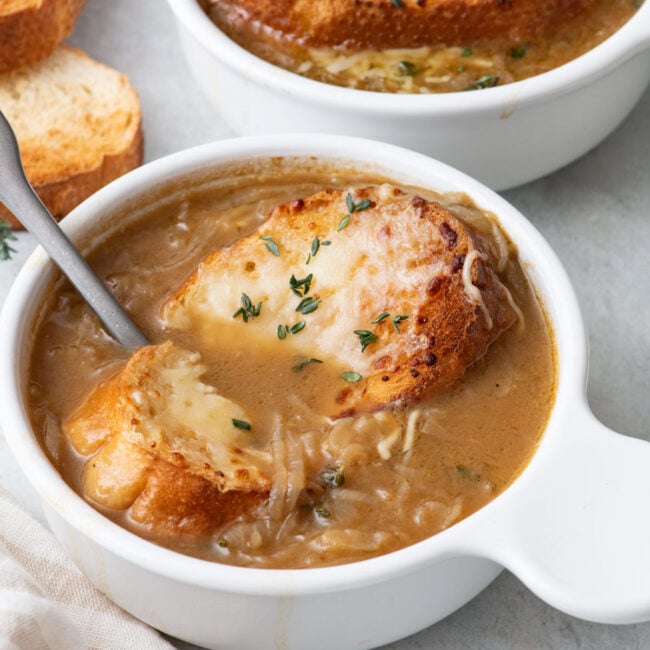 Spoon cutting into cheese bread and scooping some French onion soup up.