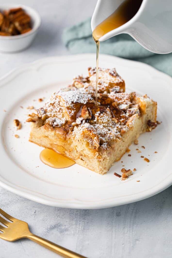 Close up shot of slice of easy french toast casserole with maple syrup getting poured on top.