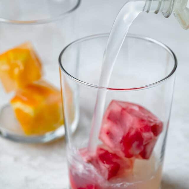 Pouring limeade into a cup with fruit cubes