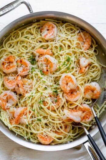 Large skillet of garlic butter shrimp pasta with serving spoon and fork in skillet