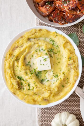 Roasted Garlic Mashed Potatoes in a large serving bowl with a side of smashed sweet potatoes nearby.