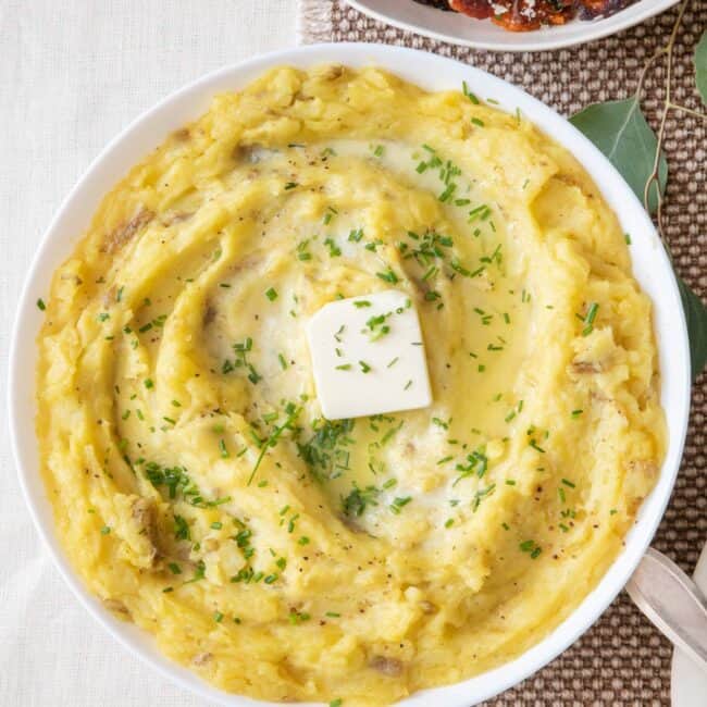 Roasted Garlic Mashed Potatoes in a large serving bowl with a side of smashed sweet potatoes nearby.