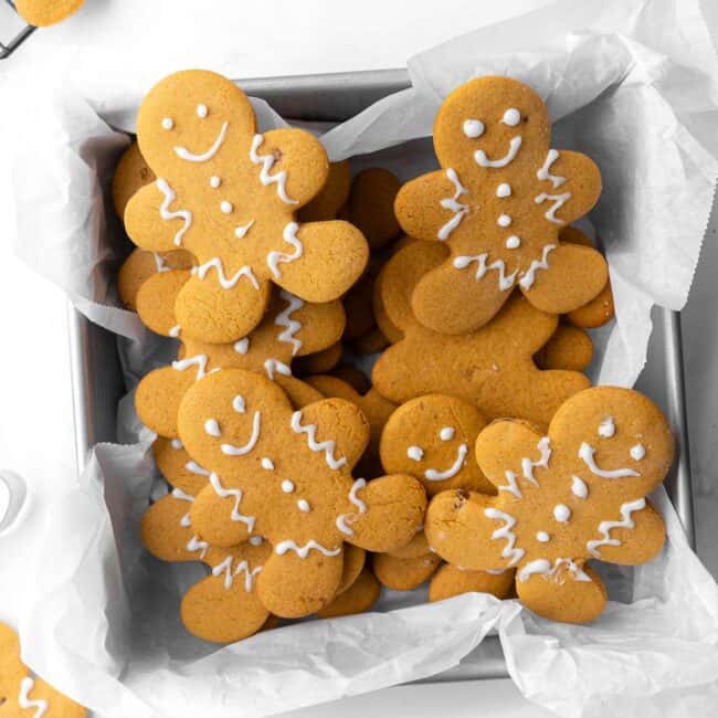 Gingerbread cookies stack in a parchment lined square tin.